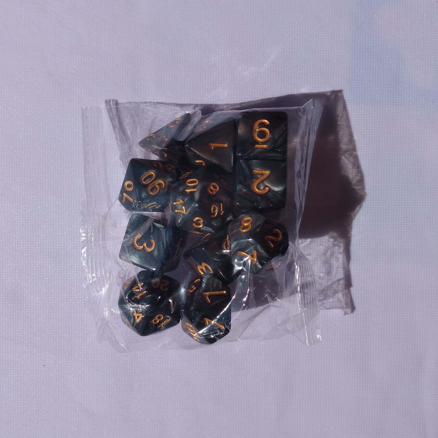 "Lot de 11 dés noir nacré avec chiffres dorés – Parfait pour jeux de rôle et jeux de société. Inclut différents types de dés (D4, D6, D8, D10, D12, D20) pour toutes vos aventures ludiques."